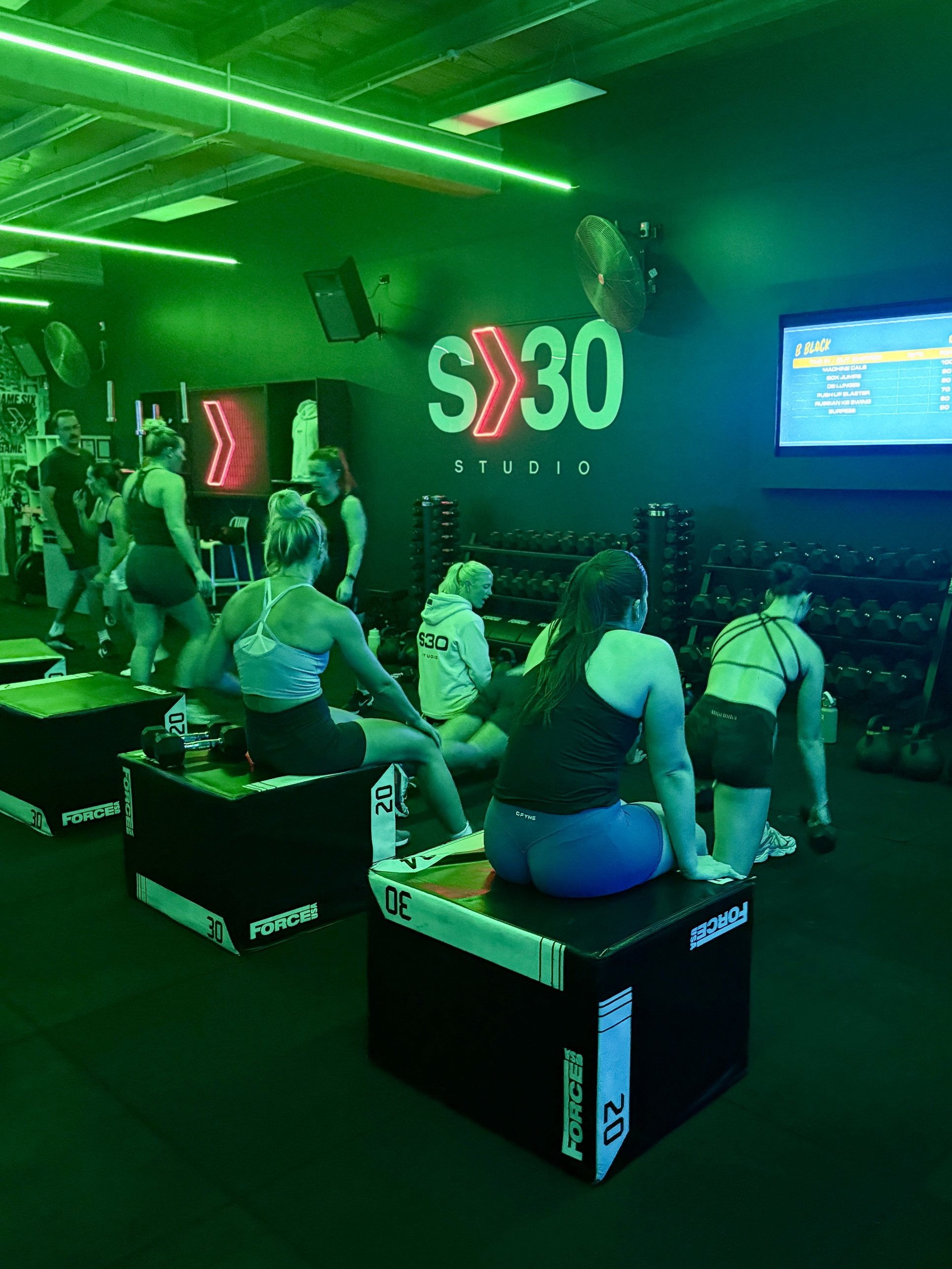 Members resting on plyo boxes under the S30 Studio sign